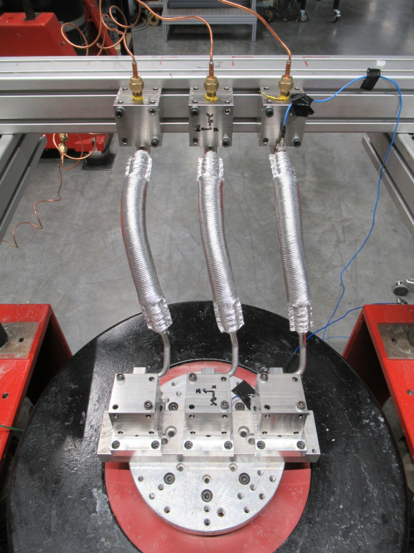 Three refrigerant lines are mounted side by side on an electrodynamic shaker. There is a pressurized gas connection at the top of each test specimen.